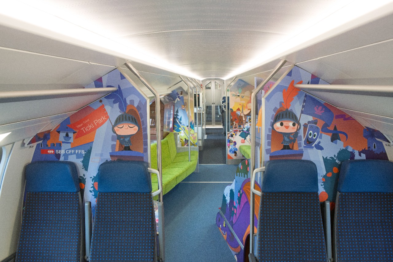 Carrozza famiglia sull’IC 200 – Prima della zona dedicata ai bambini sono disponibili posti a sedere da entrami i lati del corridoio. Nella zona di gioco si nota una fila di sedili verdi sulla sinistra.