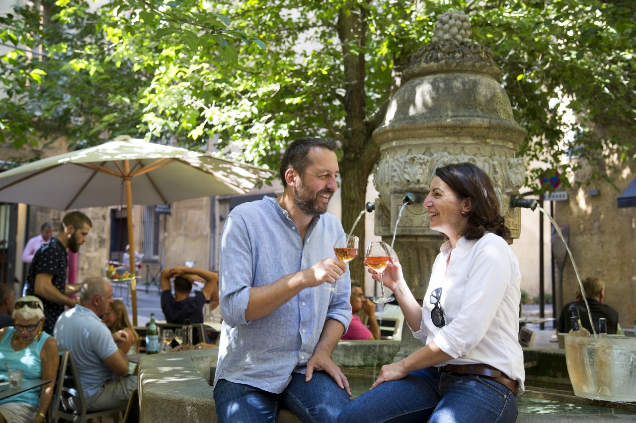 Una coppia è seduta sul bordo di una fontana e brinda con un bicchiere di vino rosé